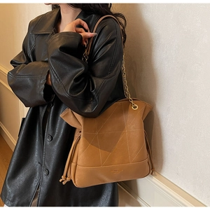 Detail of tan bucket bag with geometric quilting, gold chain strap and tassel accents