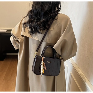 Detalle de mini bolso marrón oscuro efecto cocodrilo con colgante y bandolera