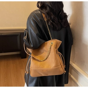 Brown quilted bucket bag with gold chain strap shown on model in stylish black leather jacket