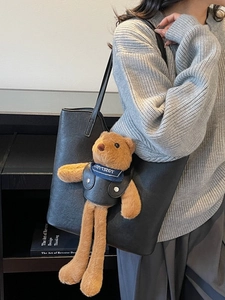 Schwarze Leder-Tragetasche mit süßem braunem Teddybär-Anhänger an der Schulter