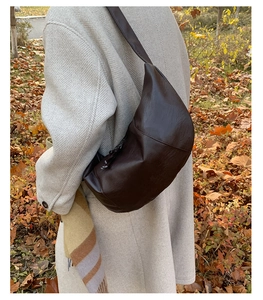 Detail of dark brown faux leather crescent bag with texture and wide strap on coat