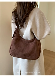 Texture détaillée d'un sac hobo en daim marron foncé porté avec un manteau minimaliste