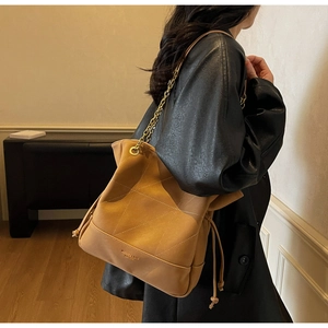 Detail of khaki suede tote bag with diamond quilting and metallic chain strap shown on model