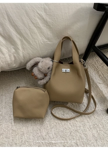 Close-up of khaki litchi grain bucket bag set with silver clasp and plush rabbit charm