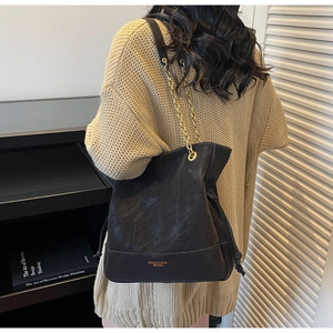 Close-up of black leather bucket bag with gold chain strap and drawstring detail
