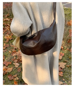 Detail of dark brown leather crescent bag with vintage texture on autumn coat