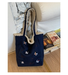 Dettaglio della borsa tote in pelle scamosciata blu navy con bordo in peluche bianco e ricami