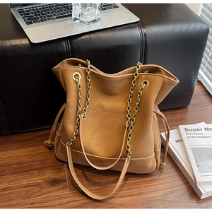Detail of camel brown tote bag with V-shaped quilting and gold chain strap in office setting