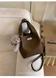 Detailed view of dark brown pebbled leather bucket bag with silver lock and plush bear charm