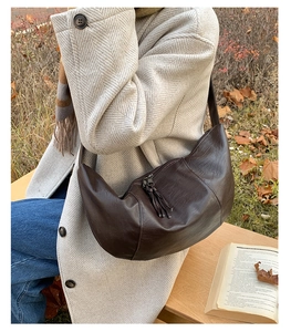 Detail of vintage brown crescent bag with fringe zippers shown on a beige winter coat