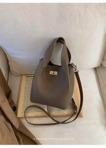 Detailed macro view of dark khaki lychee leather bucket bag with metallic twist lock on sofa