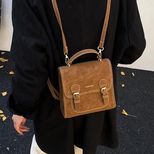 Detail of vintage brown satchel with flap and adjustable strap worn over a black coat