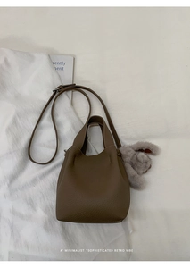 Detail of dark brown leather bucket bag with cute plush rabbit charm on magazine background