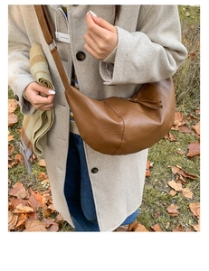 Brown faux leather dumpling bag shown crossbody on model in autumn outdoor setting