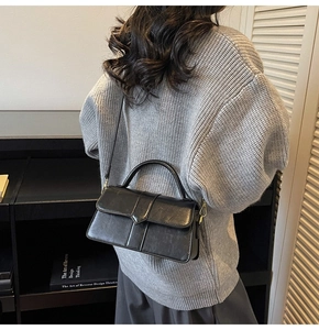 Fashionable black leather handbag shown on model against a modern interior bookshelf