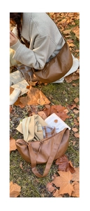 Close-up of brown crescent moon bag with tassel and wide strap on autumn grass background