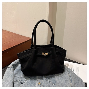 Detailed close-up of a black suede tote bag with a golden metal buckle and leather handles