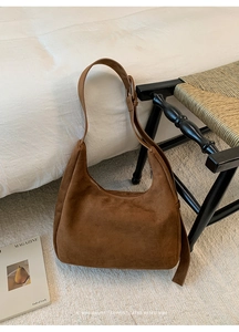 Detail of a brown suede hobo bag with adjustable strap on a minimalist indoor background