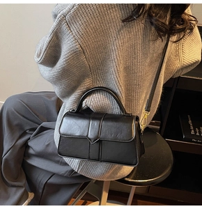 Model wearing black matte leather crossbody bag with V-shaped flap and gold hardware detail