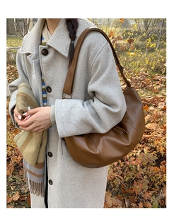 Brown leather dumpling bag with vertical stitching and tassels on a fall coat background