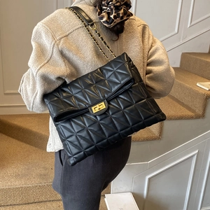 Gros plan d'un sac cabas noir matelassé avec bandoulière chaîne dorée porté à l'épaule