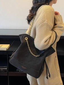 Classic black suede bucket bag with gold chain strap and drawstring shown on a model