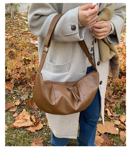 Brown PU leather crescent bag featuring pebble texture and tassel detail on an outdoor model