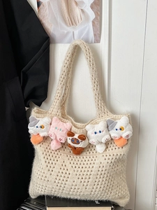 Chic hollow knit tote bag in cream with cute plush cat doll charms hanging on a wooden door