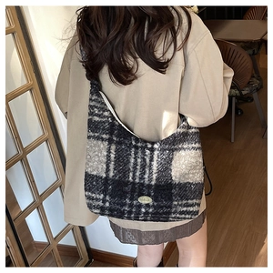 Close-up of winter plaid tote bag with handmade label worn by model in a cozy cafe