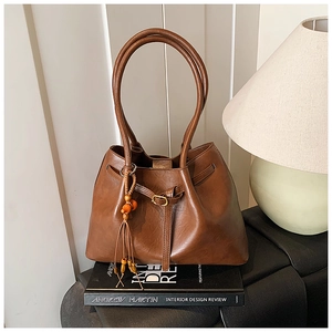Détail d'un sac cabas vintage en cuir marron foncé avec un pompon en perles de bois