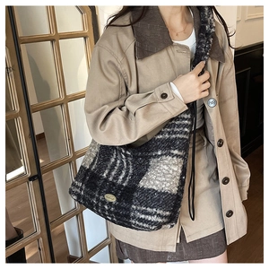 Close-up of black and white tweed tote bag featuring a premium gold oval logo plaque