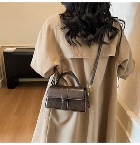 Detailed view of a vintage dark brown leather crossbody bag styled with a khaki trench coat