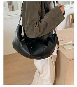 Detail of a large black leather crescent bag showing slouchy texture and wide strap