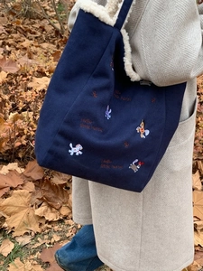 Borsa tote blu scuro ricamata con fodera in pile bianco in un ambiente autunnale