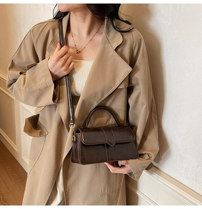 Detail of dark brown vintage crossbody bag with V-buckle strap on a stylish trench coat