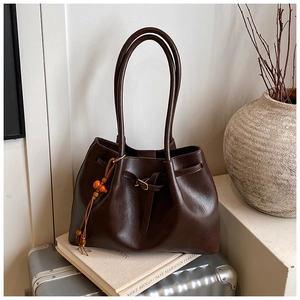 Détail d'un sac cabas marron brillant avec pompon perlé posé sur une valise argentée