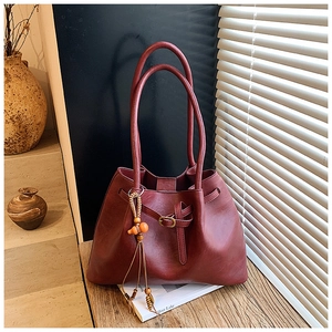 Vue détaillée du sac cabas bordeaux avec pompons en bois et texture polie brillante