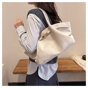 Detailed view of oatmeal suede tote bag with metallic clasp worn by a model in soft light