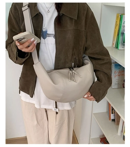 Detail of a beige half-moon crossbody bag shown in a stylish indoor lifestyle setting