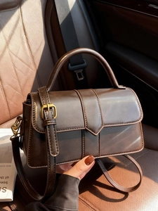 Deep brown leather crossbody bag with V-shaped flap and gold hardware on car seat