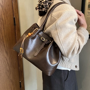 Détail du sac cabas en cuir marron vintage avec un gland décoratif et perles oranges