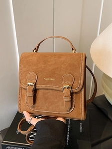 Vintage caramel brown satchel bag with buckle straps on a fashion book background