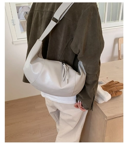 Close-up of beige half-moon crossbody bag with leather tassels and wide adjustable strap