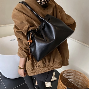 Détail d'un sac cabas noir vintage avec une breloque décorative en bois et un gland