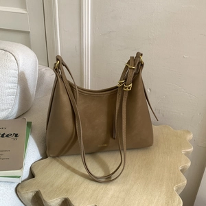 Detail of tan faux leather shoulder bag with gold branding on an artistic wooden stool