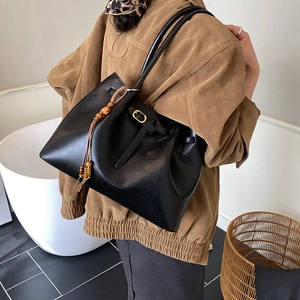 Détail d'un cabas vintage en cuir noir avec breloque en perles de bois porté par un mannequin