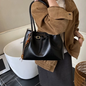 Détail du sac cabas en cuir noir vintage avec boucle dorée et gland en bois perlé