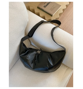 Detail of black crescent shoulder bag featuring wide strap and dual zippers on a sofa