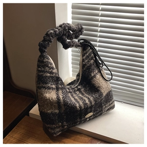 Detail of checkered tweed hobo bag with woven handle and handmade metal tag on windowsill