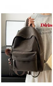 Detail of vintage dark brown backpack featuring contrasting white stitching and a plush ball charm